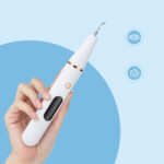 Détartreur dentaire blanc tenu par quelqu'un, fond bleu.