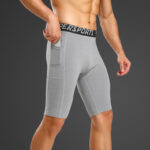 On voit un homme torse-nu avec un short de compression gris avec poches latérales.