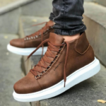 Paire de chaussures orthopédiques homme marrons et épaisses en simili cuir sur un homme en jean