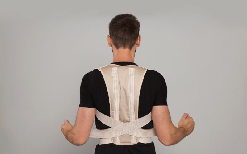 Homme de dos portant un correcteur de posture, il règle les sangles à scratch.