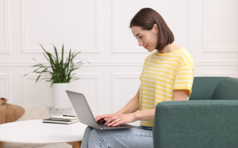 Jeune femme assise sur un canapé vert avec un ordinateur portable sur les genoux.